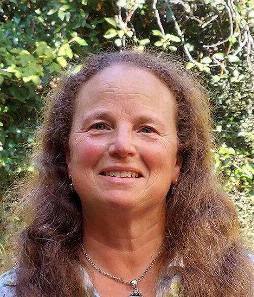 A headshot of a smiling woman in front of some bushes